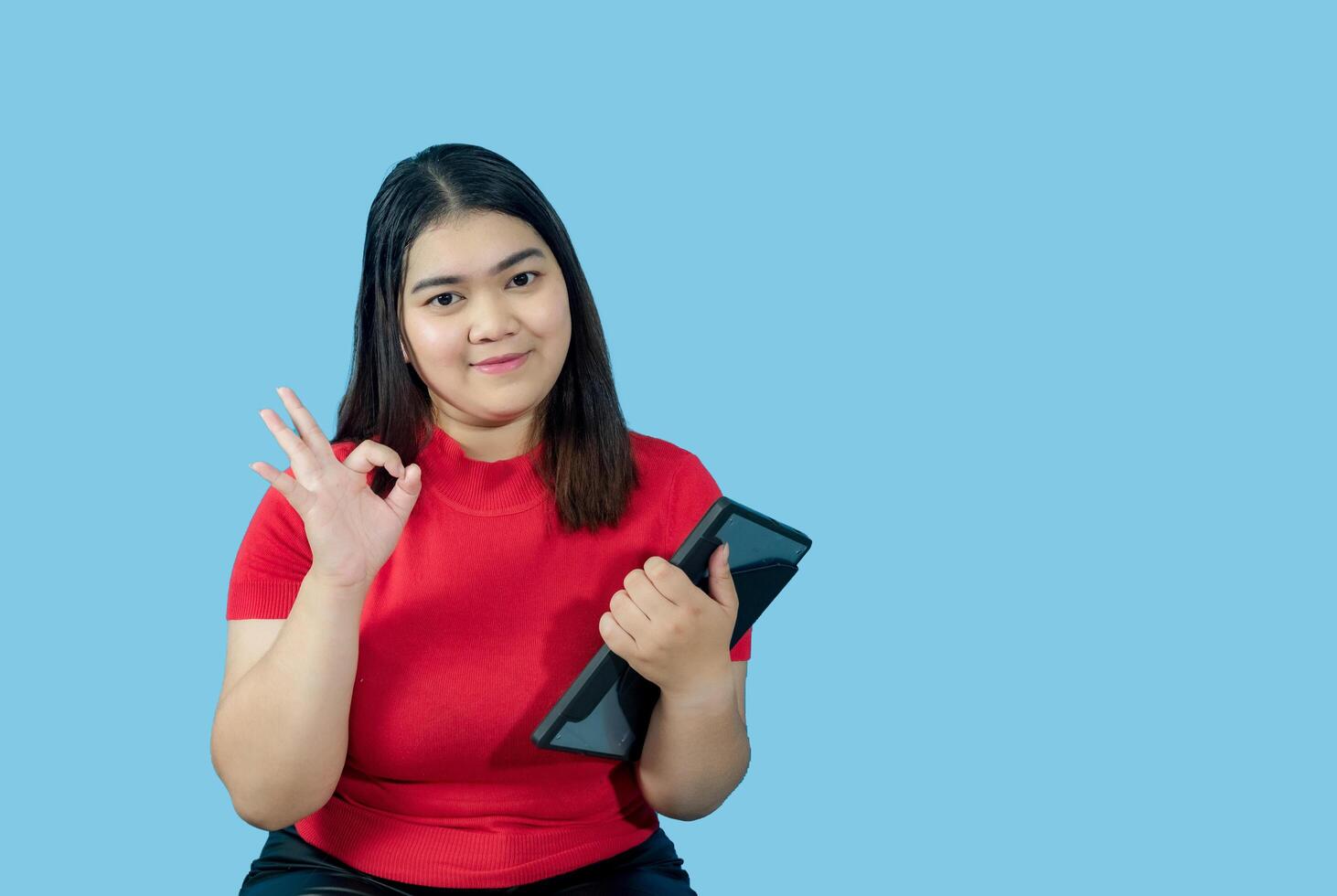 retrato negocio niña joven mujer asiático gordito grasa linda hermosa bonito uno persona vistiendo rojo camisa en oficina participación digital tableta y sonriente en pie con Copiar espacio en aislado azul suelo negro foto