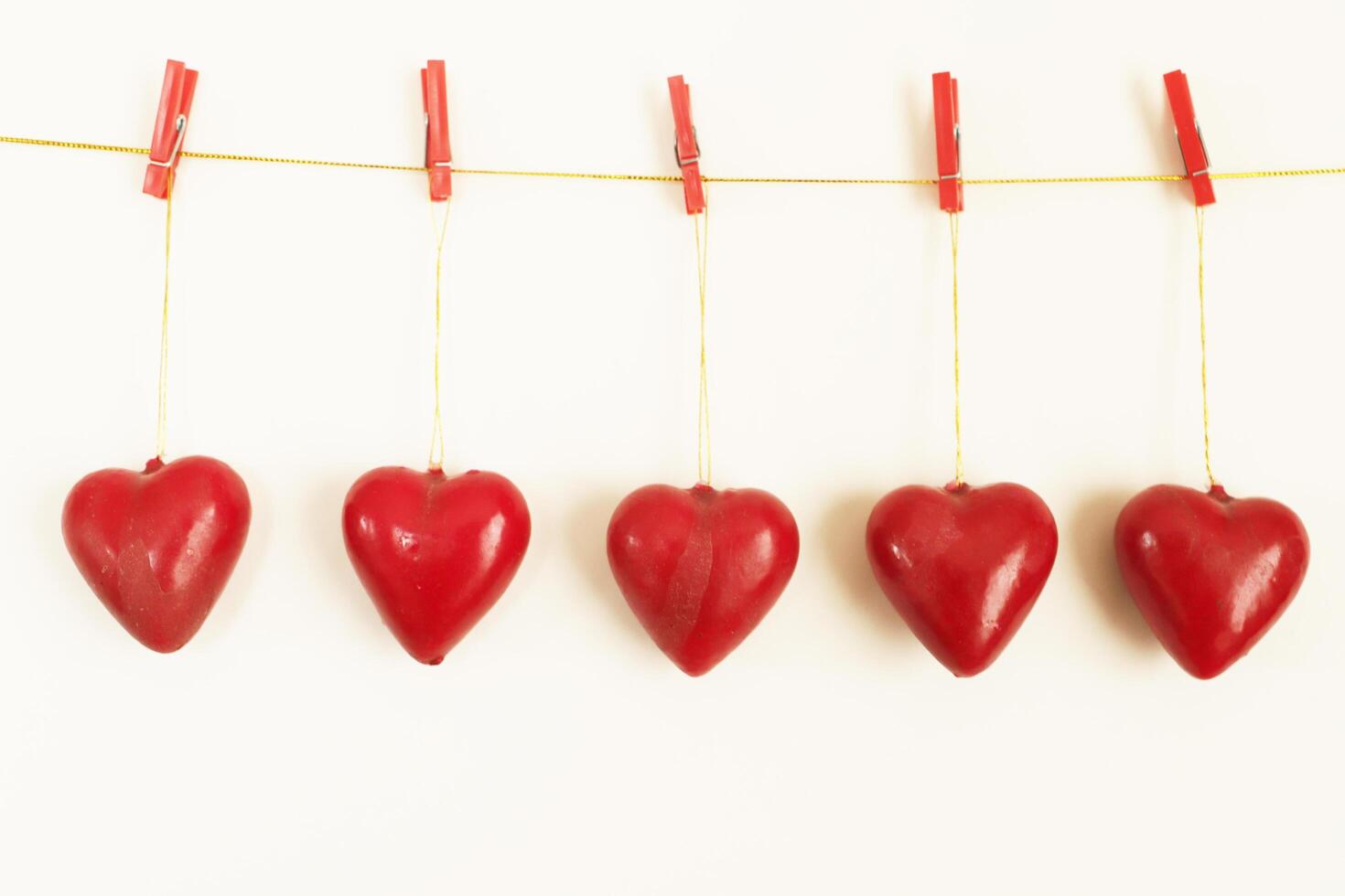 five red hearts hang from a line with pegs. white background photo