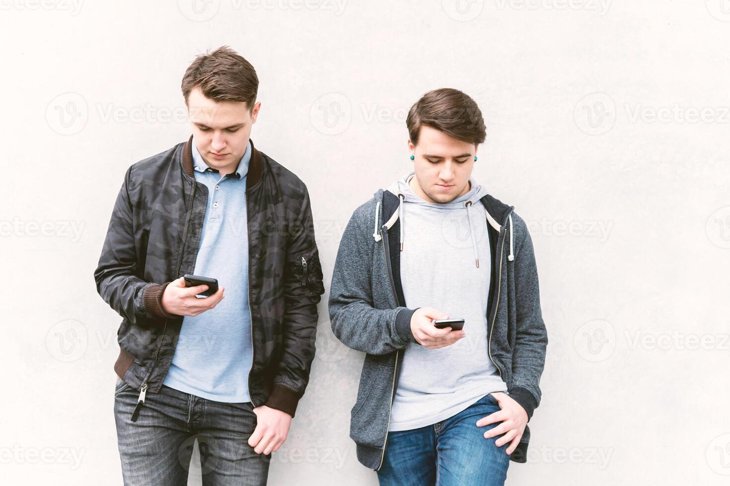 two antisocial mobile phone addicted male teenagers looking at their smartphone photo