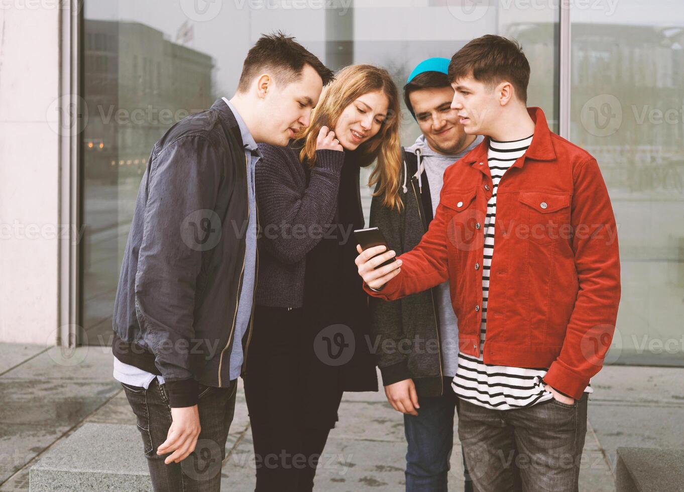 young man showing something on his mobile phone to a group of teenage friends photo