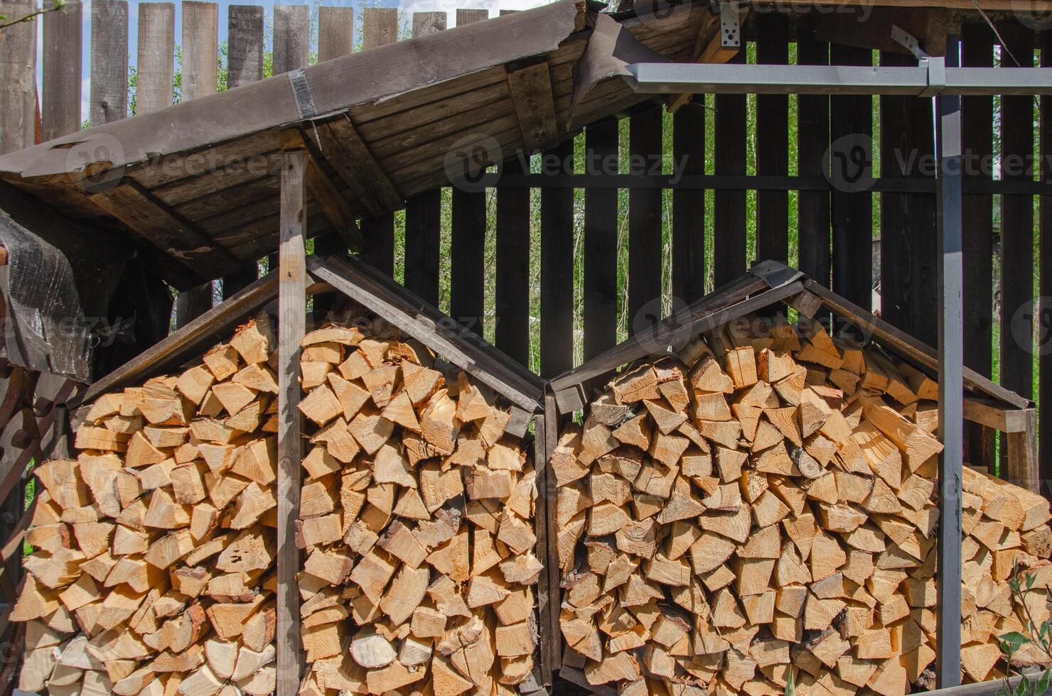 Firewood is prepared for the cold and stacked under a canopy photo