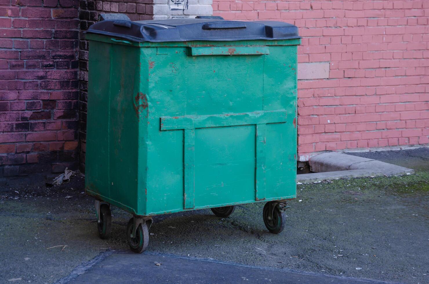A garbage container stands against a wall closed photo
