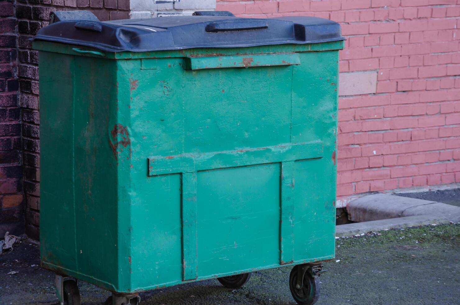 A garbage container stands against a wall closed photo