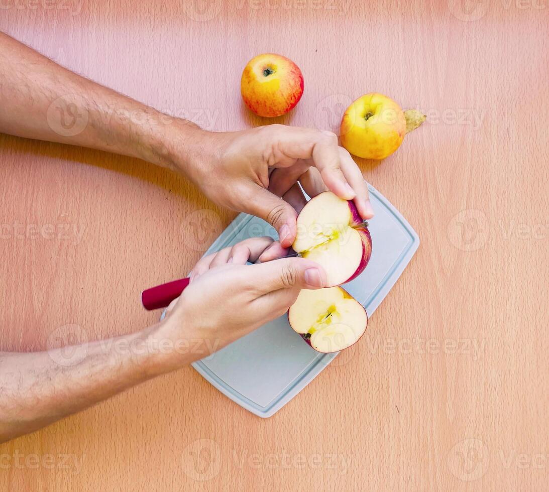 Close up male hands cut an apple into slices. Top view of preparing fruits over kitchen table. photo