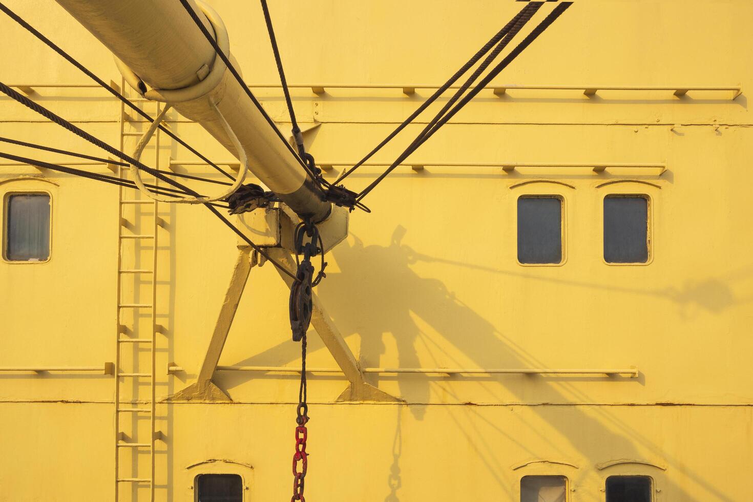 Part of the old boom crane with rusty hoist and wire rope sling in yellow nautical ship, vehicle in sea transportation concept photo