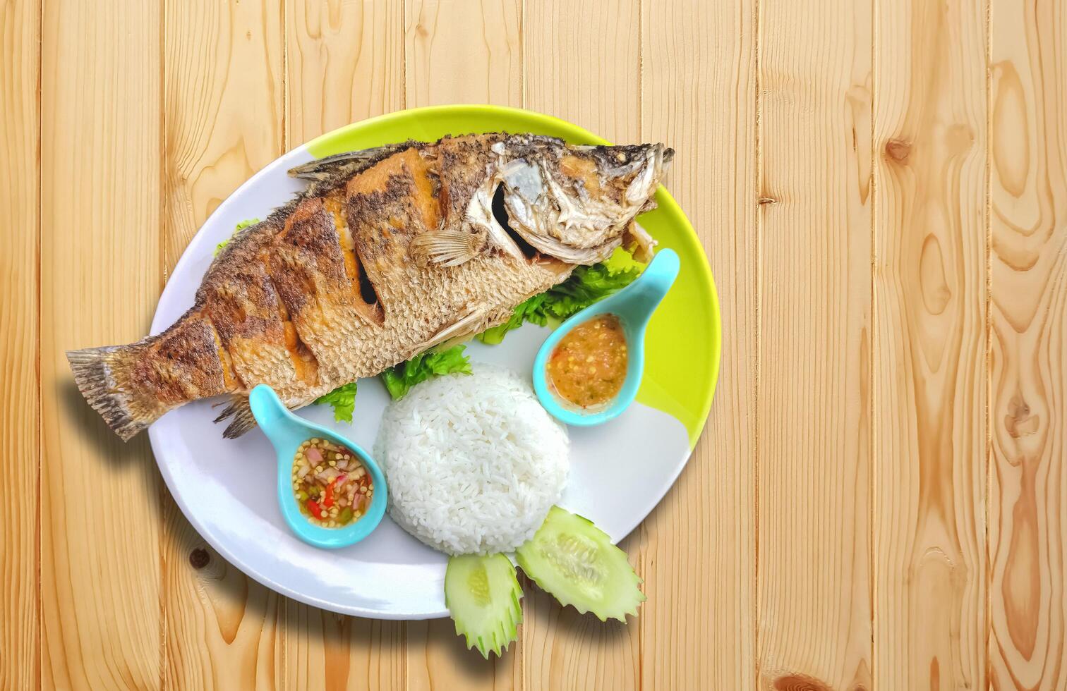 Deep fried Sea bass with fish sauce and steamed rice with Thai seafood sauce on wooden table top, top view with copy space photo