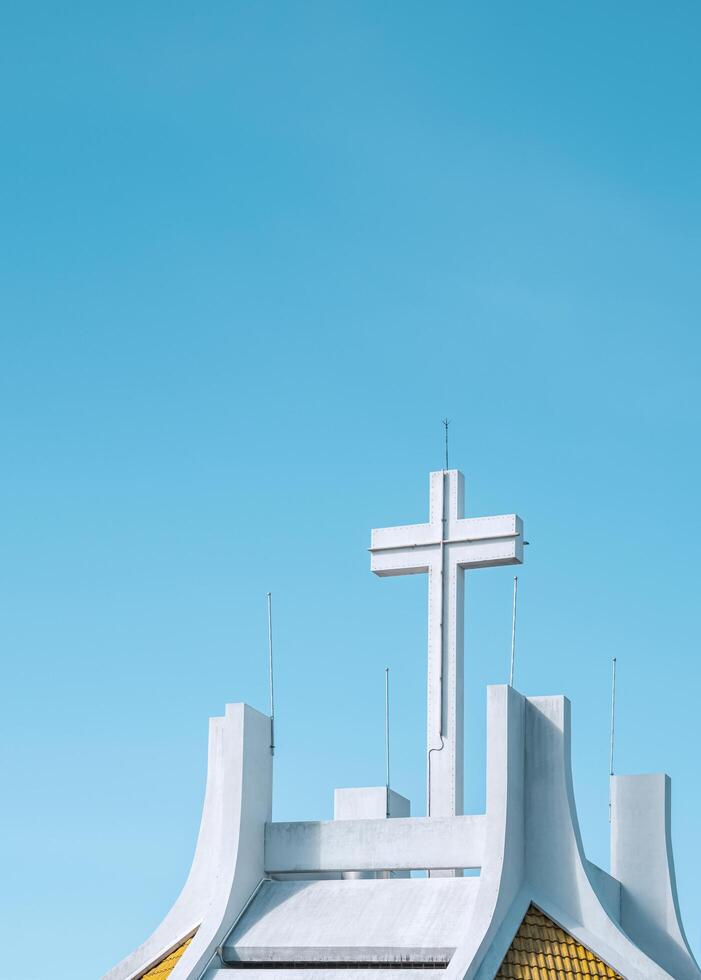 Low angle view of large cross on rooftop of white church against blue clear sky background in pastel color tone and vertical frame photo