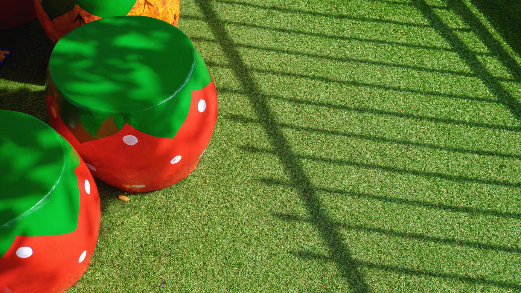 Sunlight and shadow on surface of decorative stucco garden seats in strawberry shape on artificial turf in front yard area photo