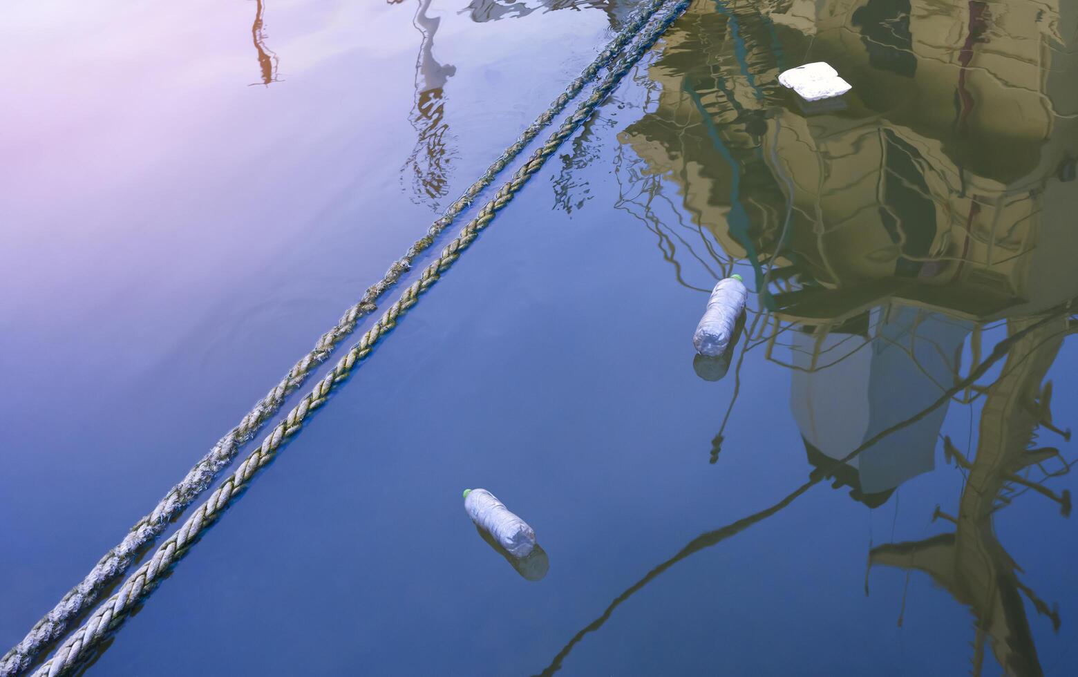 Discarded plastic rubbish bottles with foam box floating on river surface at harbor in evening time photo