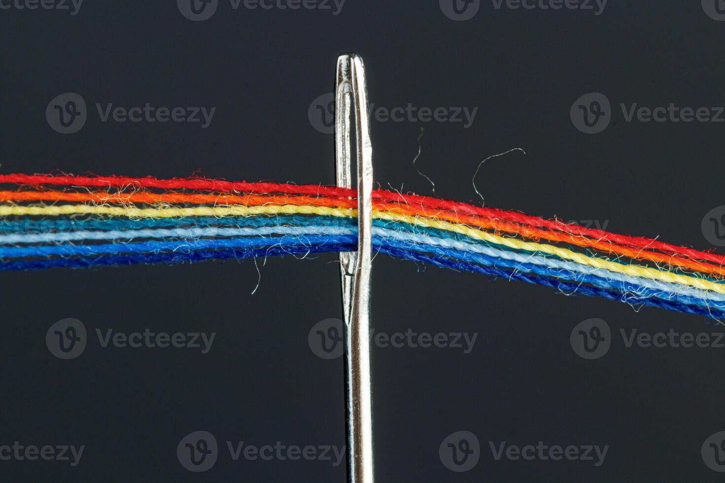 multi-colored threads for sewing in the form of a rainbow pass through an antique needle on a black background photo