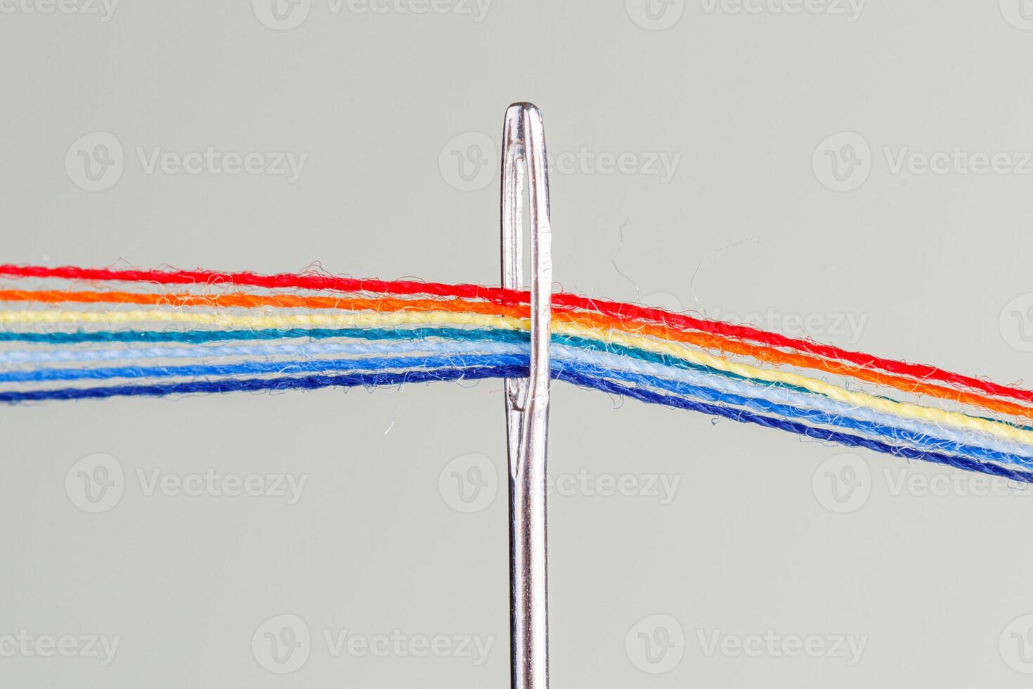 multi-colored threads for sewing in the form of a rainbow pass through an antique needle on a white background photo