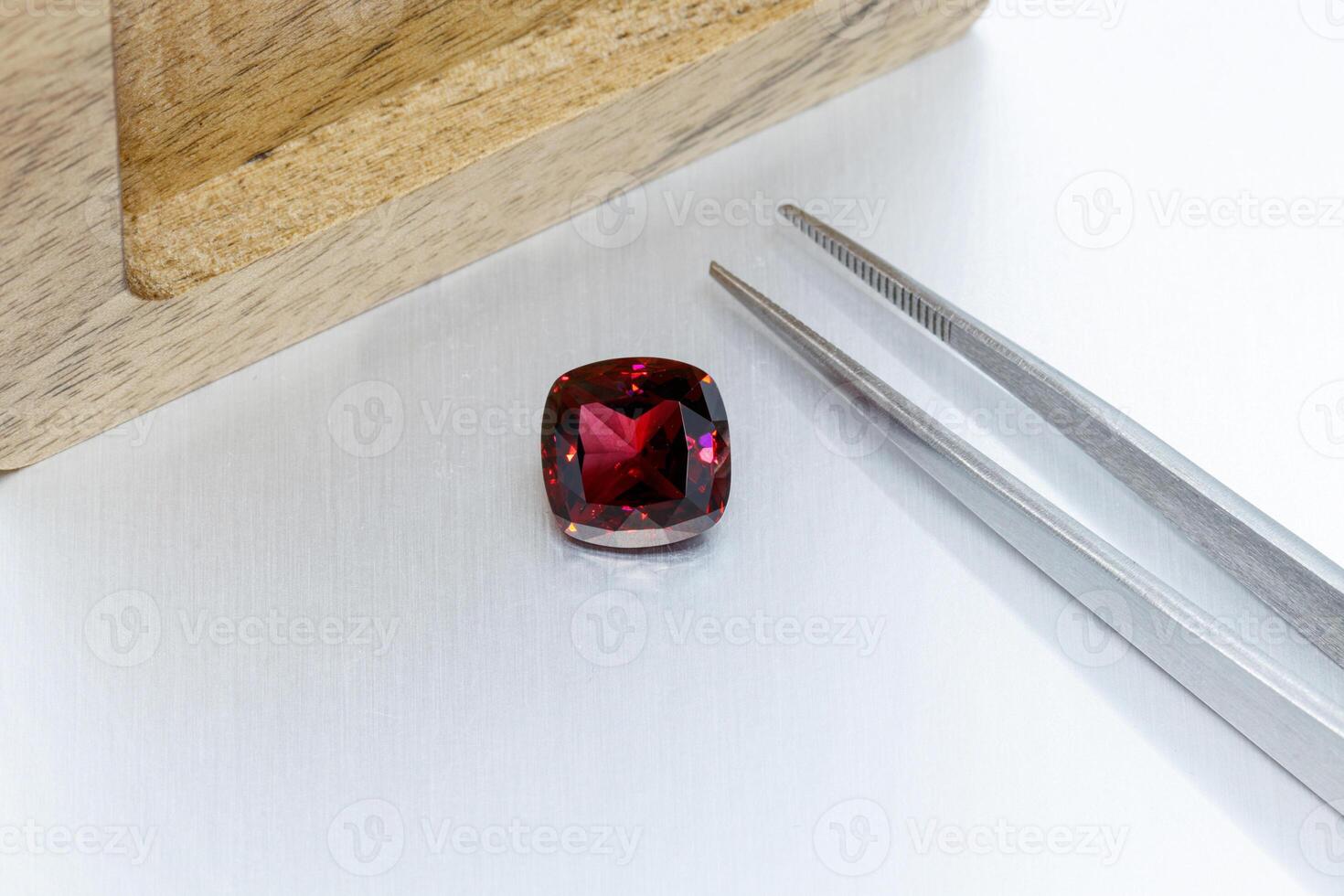 macro mineral faceted stone Garnet with tweezers on a gray background photo