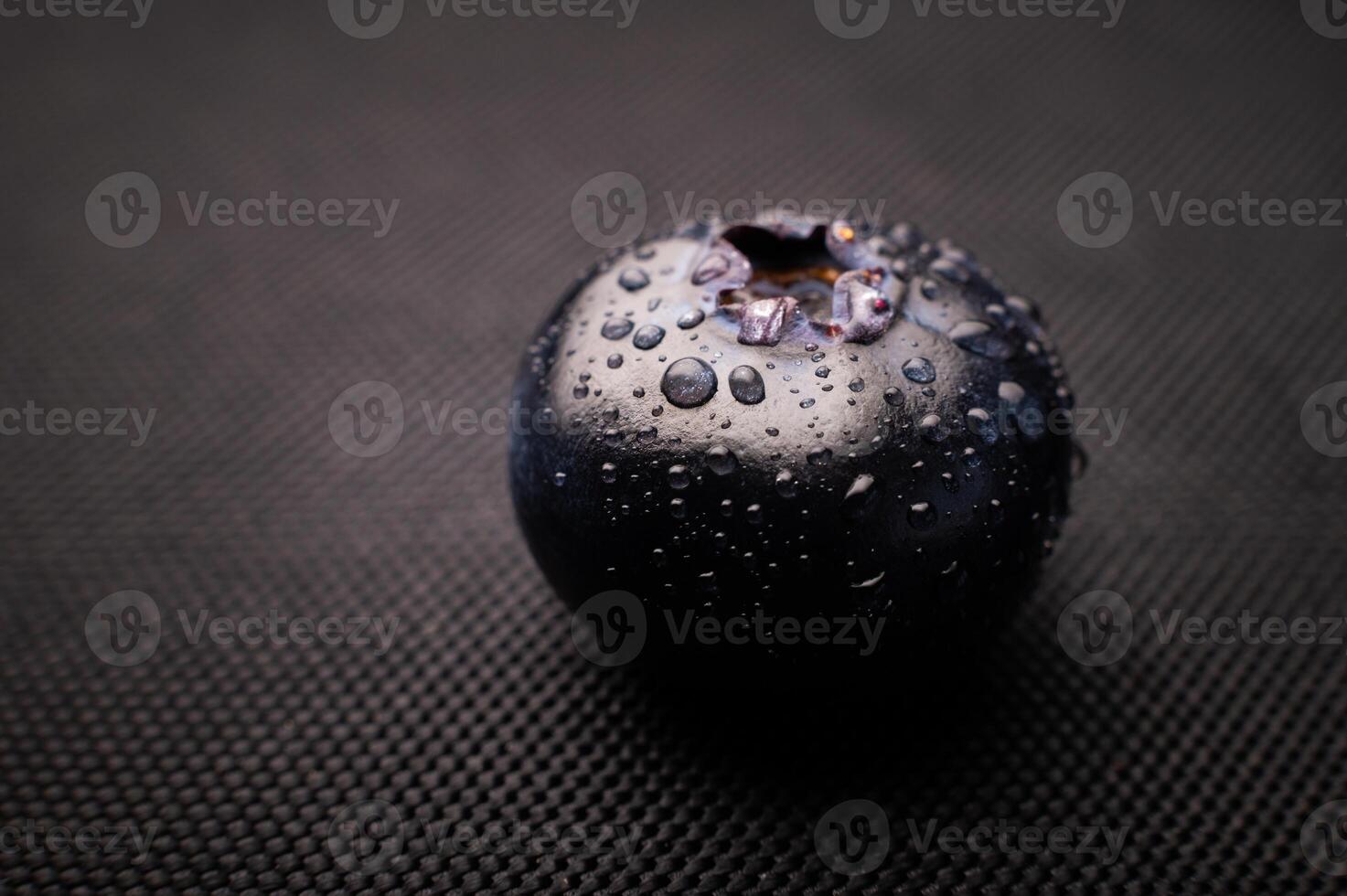 One blueberry covered with water drops on black background. Very detailed macro shoot with copy space photo