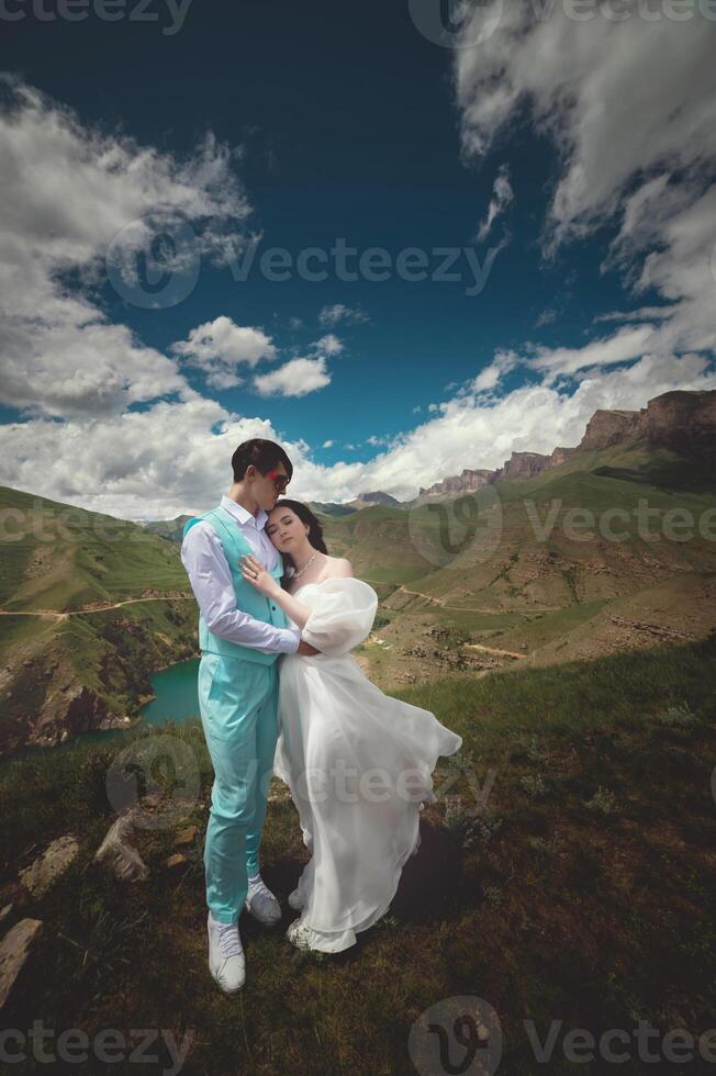 Young newlyweds, bride and groom hugging with a beautiful view of the mountains, blue sky with white clouds and green meadows in the background photo