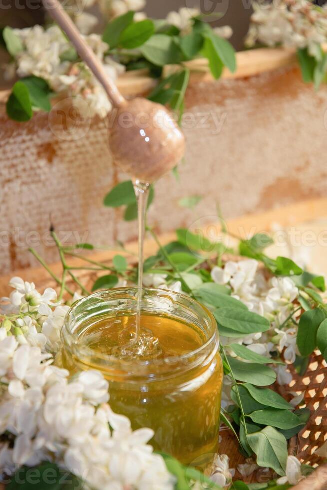 still life of a full jar of transparent yellow ocacia honey on the table against the background of wax honeycombs photo