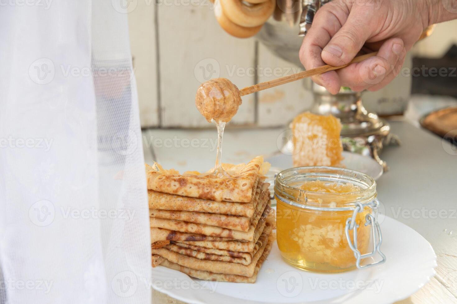 un hombre vierte miel en panqueques y bebidas té desde un samovar, ruso tradicion de celebrando maslenitsa foto