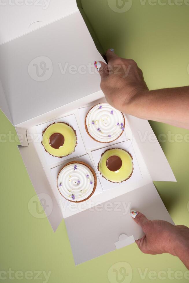 female hands open a box with different cakes dessert home delivery photo