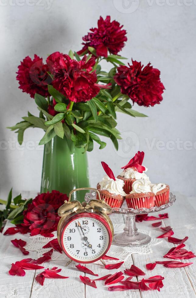 still life in English style with scarlet peonies and red velvet cupcakes with on a platter,tea time on red antique clock photo