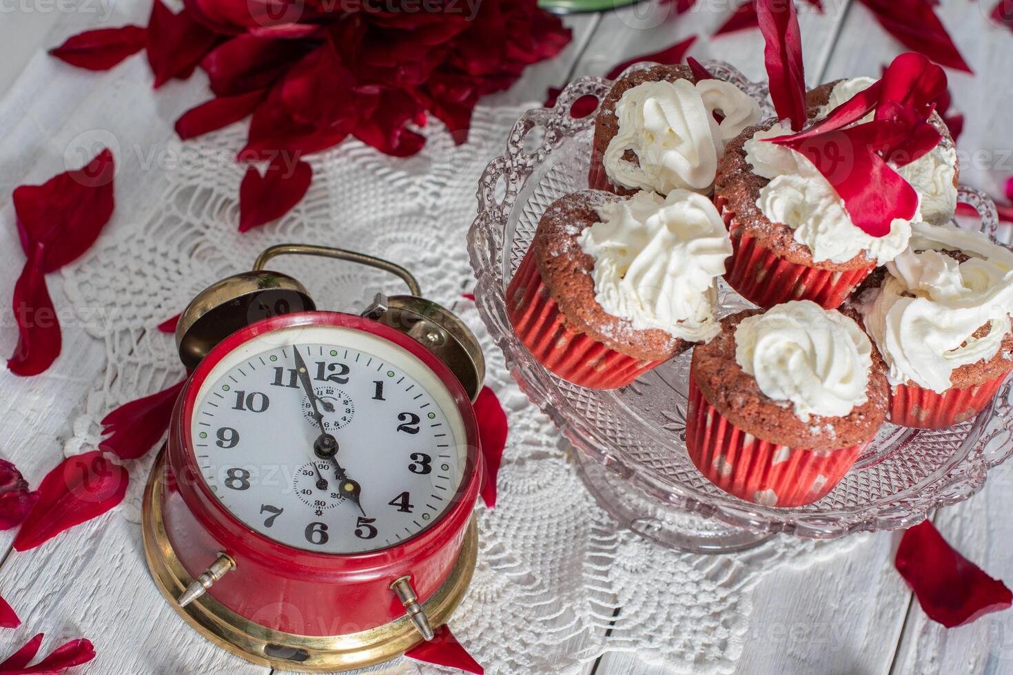 still life in English style with scarlet peonies and red velvet cupcakes with on a platter,tea time on red antique clock photo