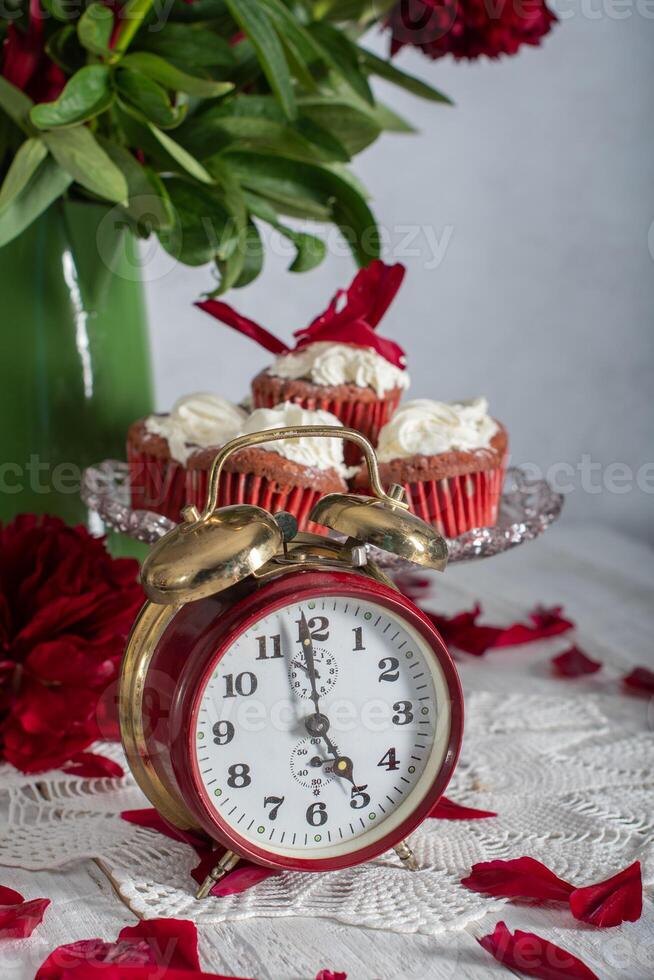 still life in English style with scarlet peonies and red velvet cupcakes with on a platter,tea time on red antique clock photo