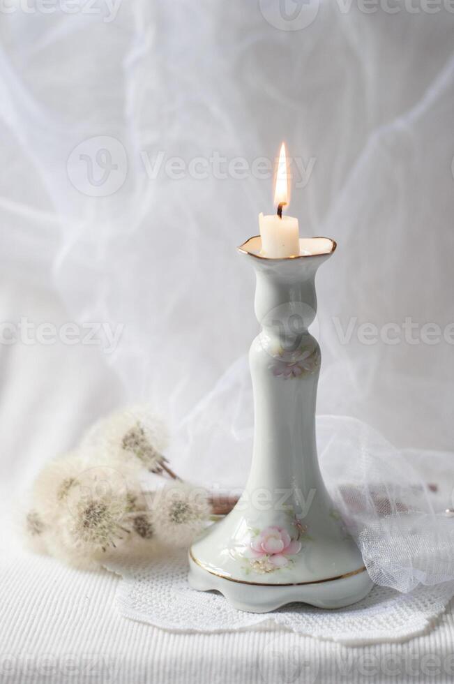 Still life with vintage porcelain candlestick and burning candle against the background of bouquet of fluffy dandelions photo