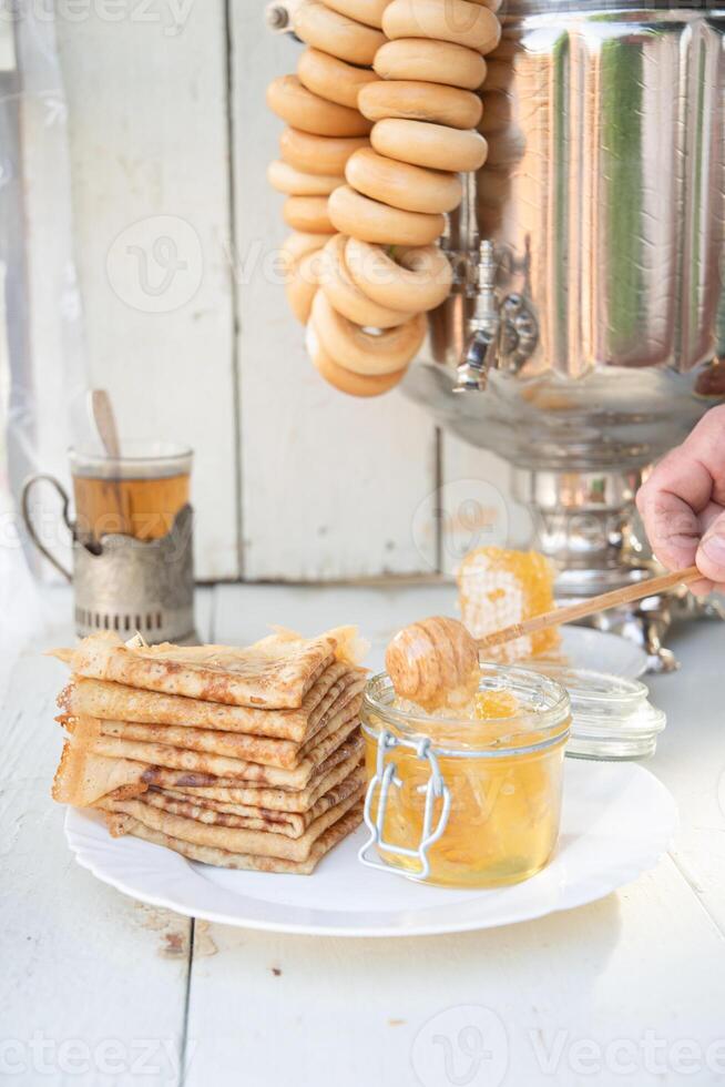 un hombre vierte miel en panqueques y bebidas té desde un samovar, ruso tradicion de celebrando maslenitsa foto