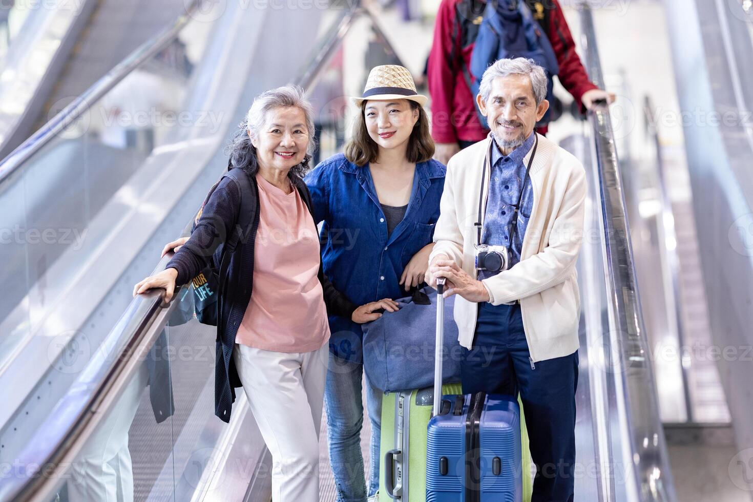 grupo de asiático familia turista pasajero con mayor padre utilizando escalera mecánica a el aeropuerto terminal para aerolínea viaje y fiesta vacaciones concepto foto