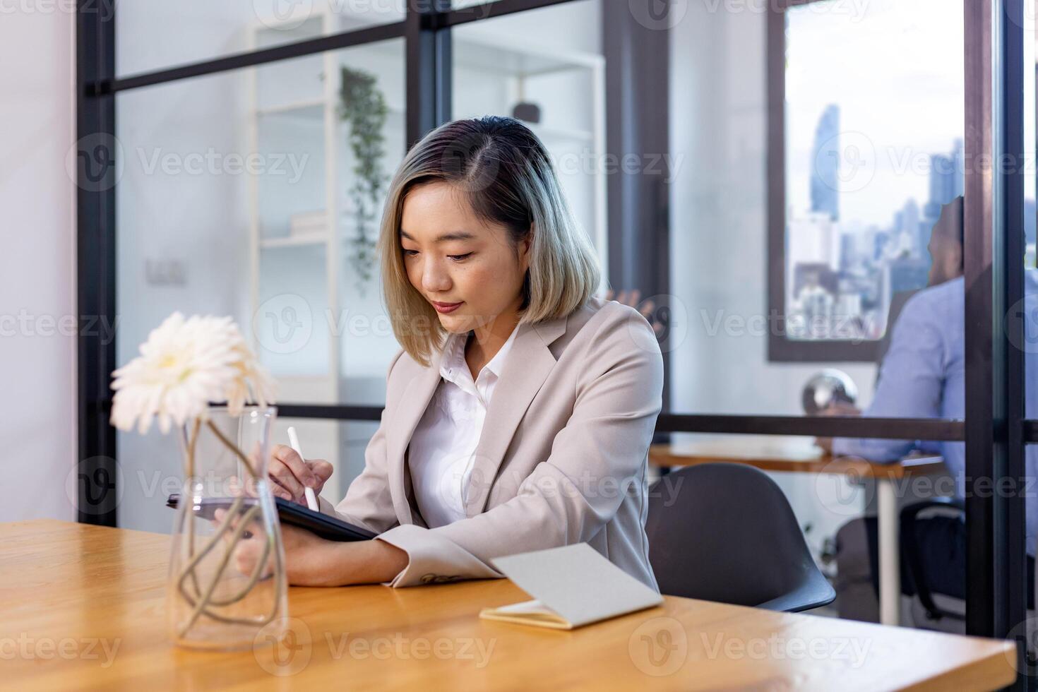 retrato de asiático negocio CEO mujer es trabajando en oficina a el mesa con digital tableta y demostración estadística gráfico demostración anual reporte y rascacielos antecedentes foto