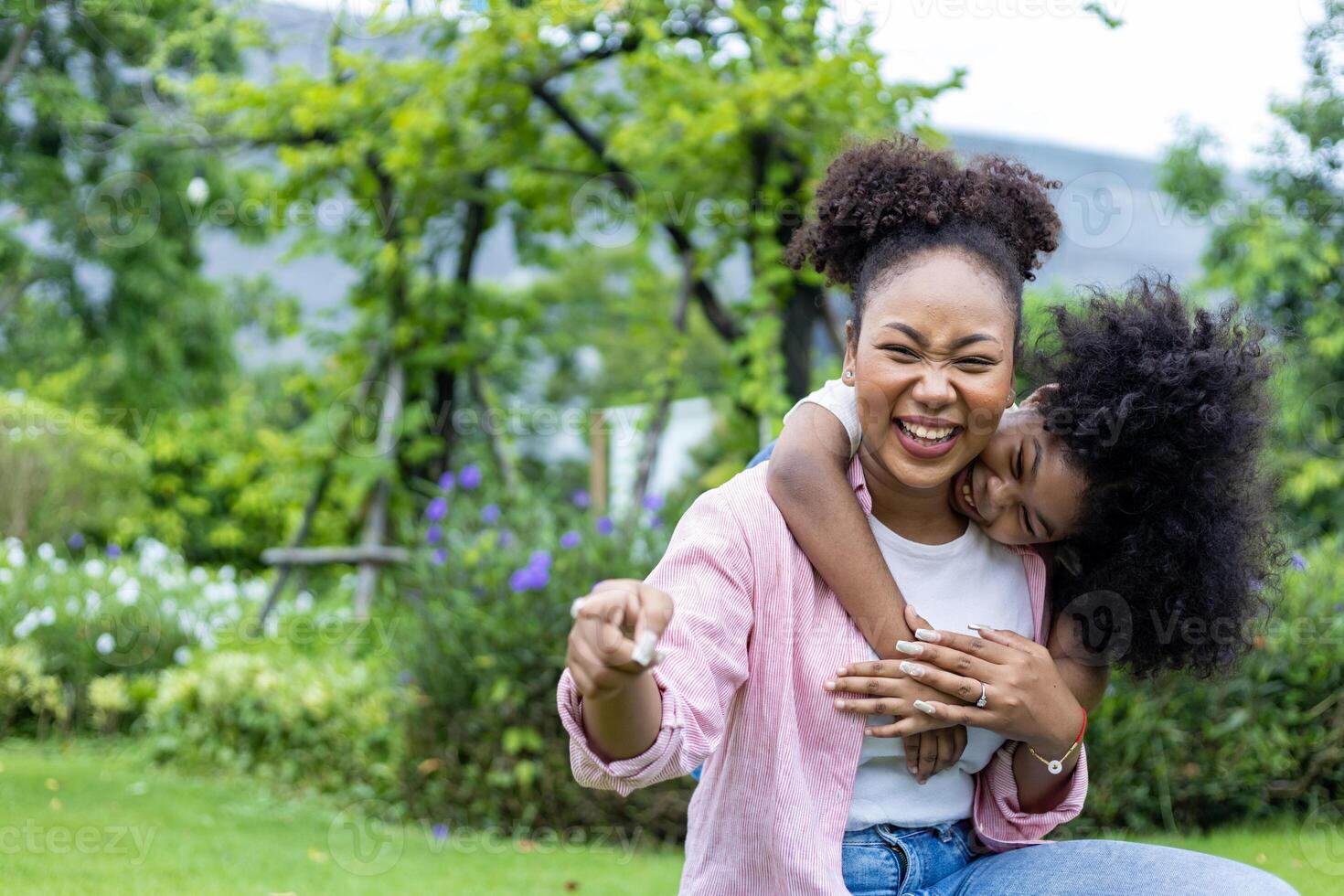 African American mother is playing piggyback riding with her young daughter while having a summer picnic in the public park for wellbeing and happiness photo