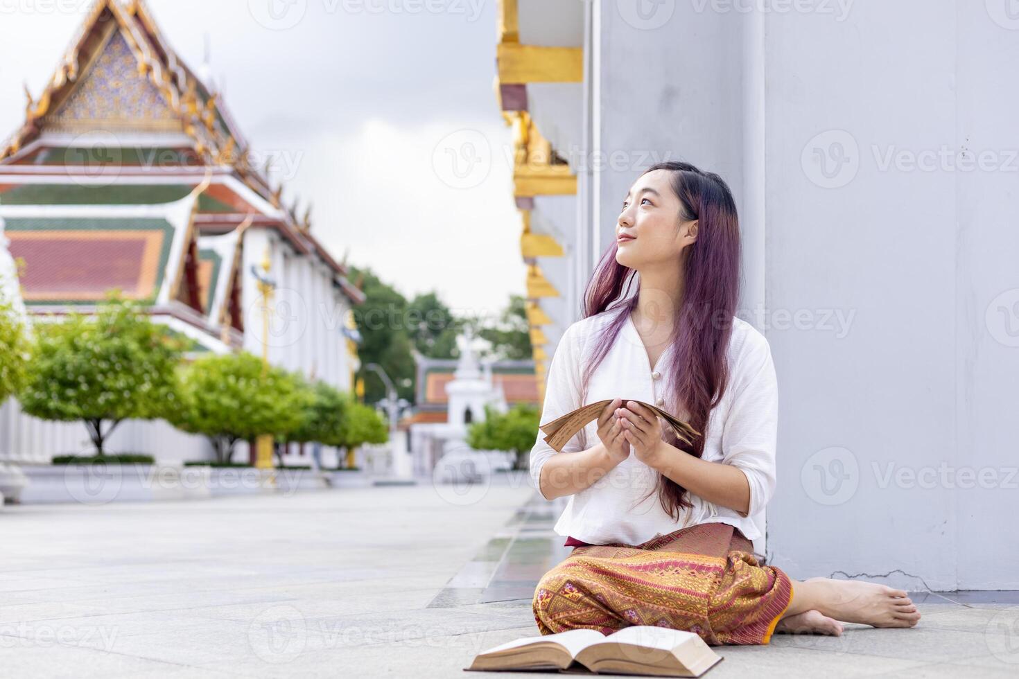 Asian buddhist woman is reading Sanskrit ancient palm leaf manuscript of Tripitaka the Lord Buddha dhamma teaching while sitting in temple on holy full moon day to chant and worship in the monastery photo