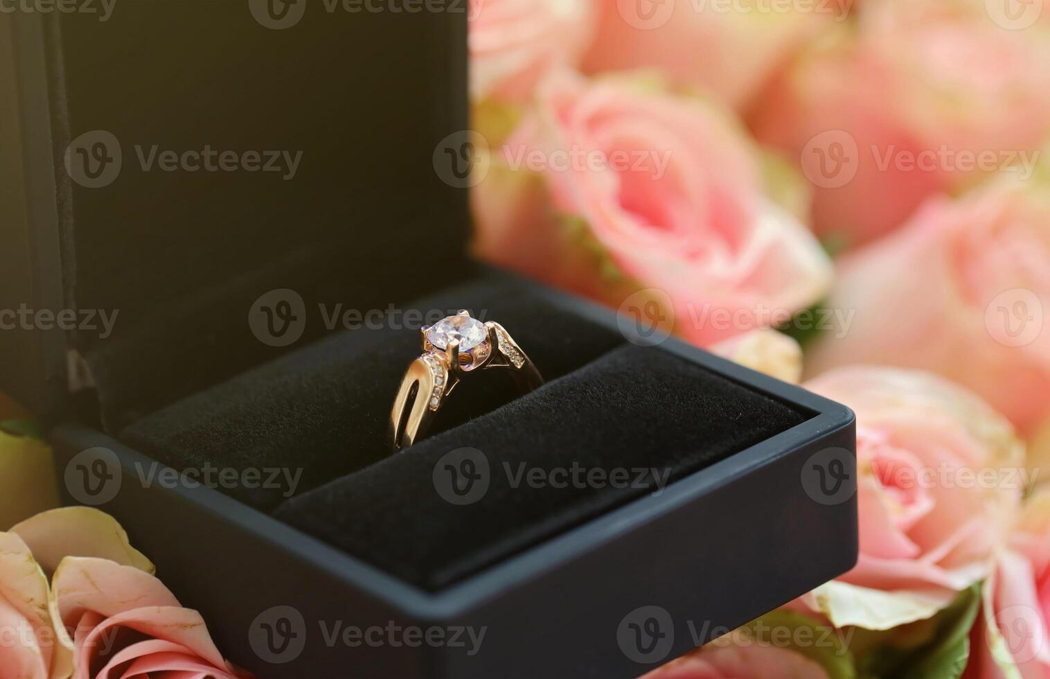 Gold diamond engagement ring in black box case among big amount of roses in big bouquet close up photo