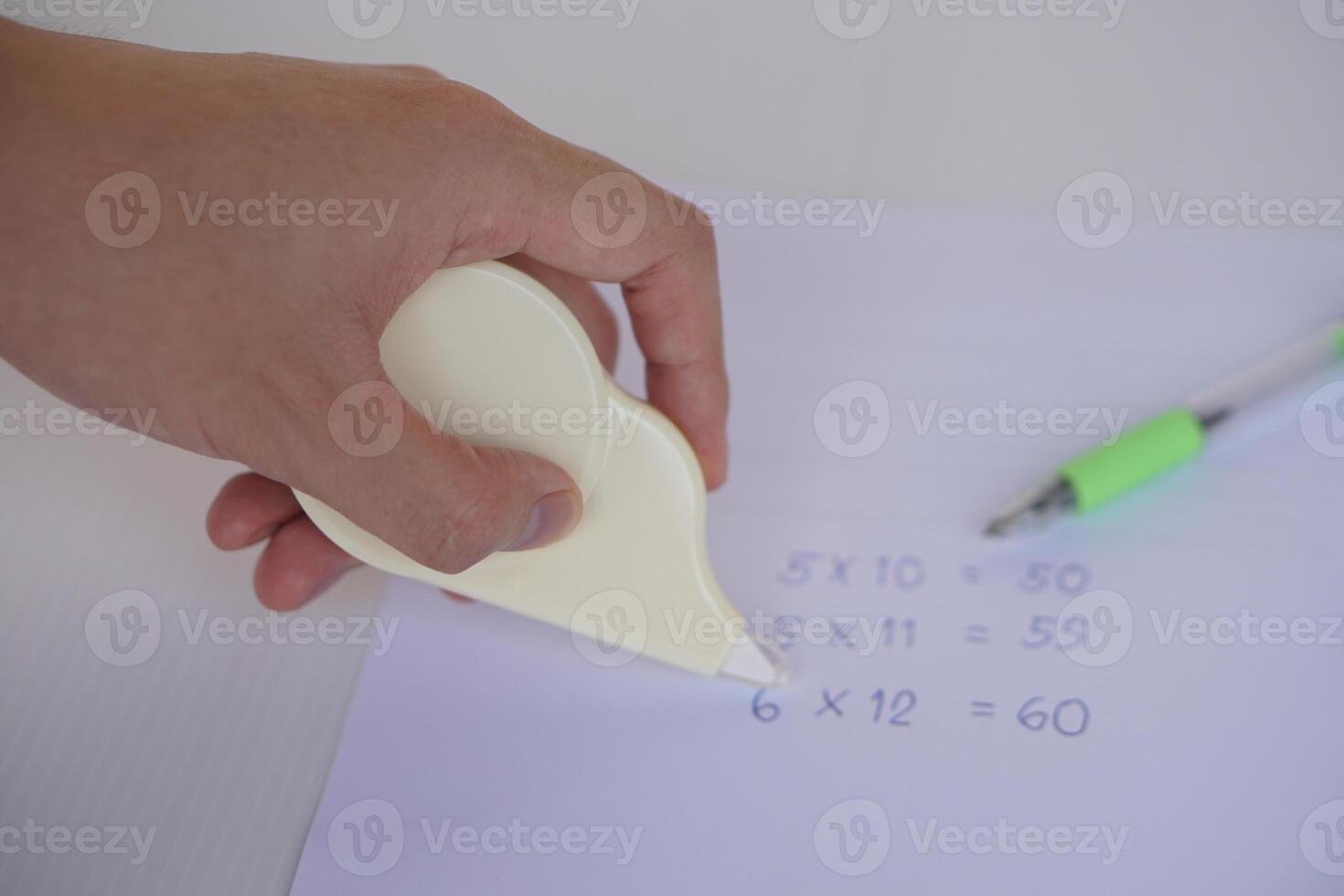 Hand use correction tape to erase incorrect numbers on paper. Concept, educational equipment, stationary item to delete or erase mistake in writing. Easy and convenient to use. photo