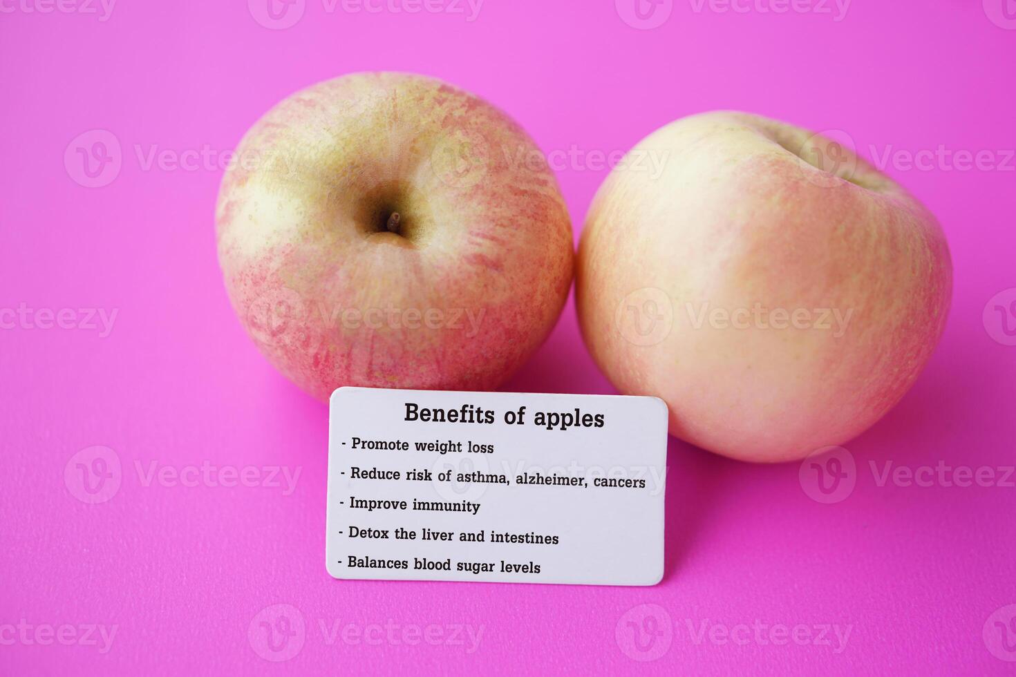 Two apples with tag of text Benefits of apples. Pink background. Concept, Apple fruits with good qualification for health. Photo for education. Teaching aid. Healthy food, fruit lesson.