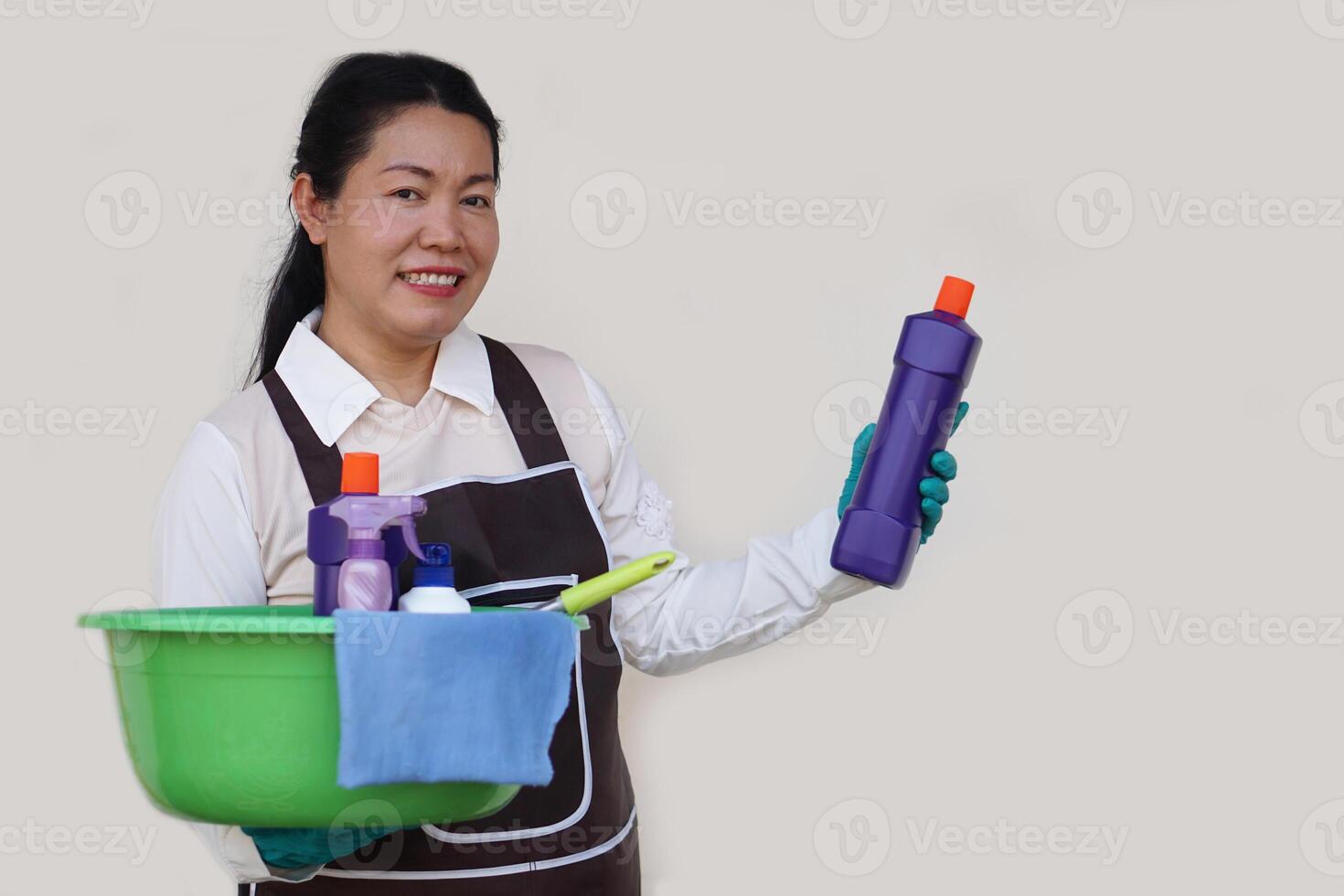 Asian woman housewife wears gloves, apron, holds bucket, bottles of cleaning liquid, alcohol spray, sanitary products and equipment for cleaning. Concept, Cleaning time for hygiene. Housekeeping. photo