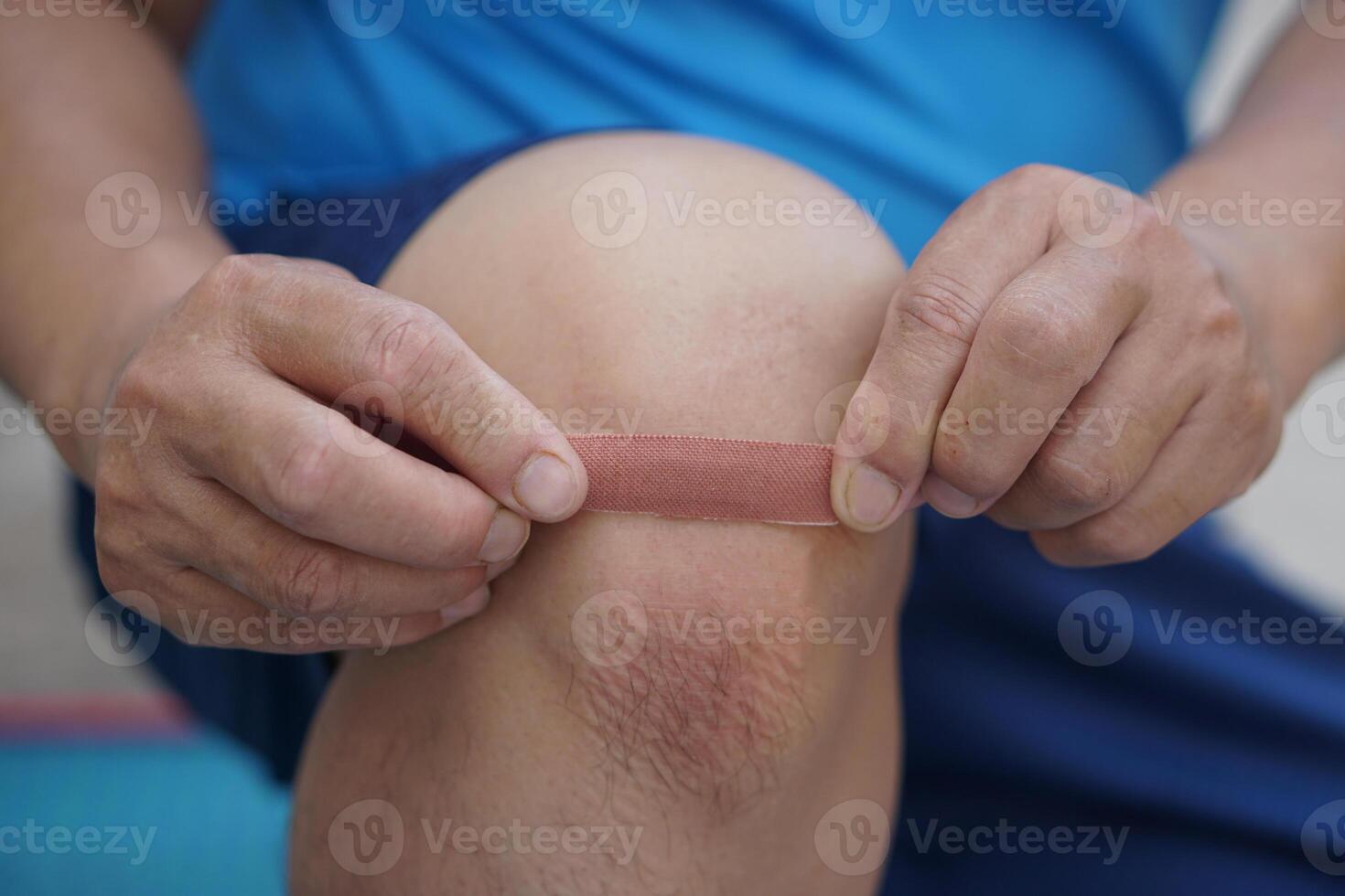Close up man uses adhesive bandage tape to cover wound on knee. Concept, first aid. Self care for injury, to protect and prevent from dirt or germs into wound by covering adhesive bandage plaster. photo