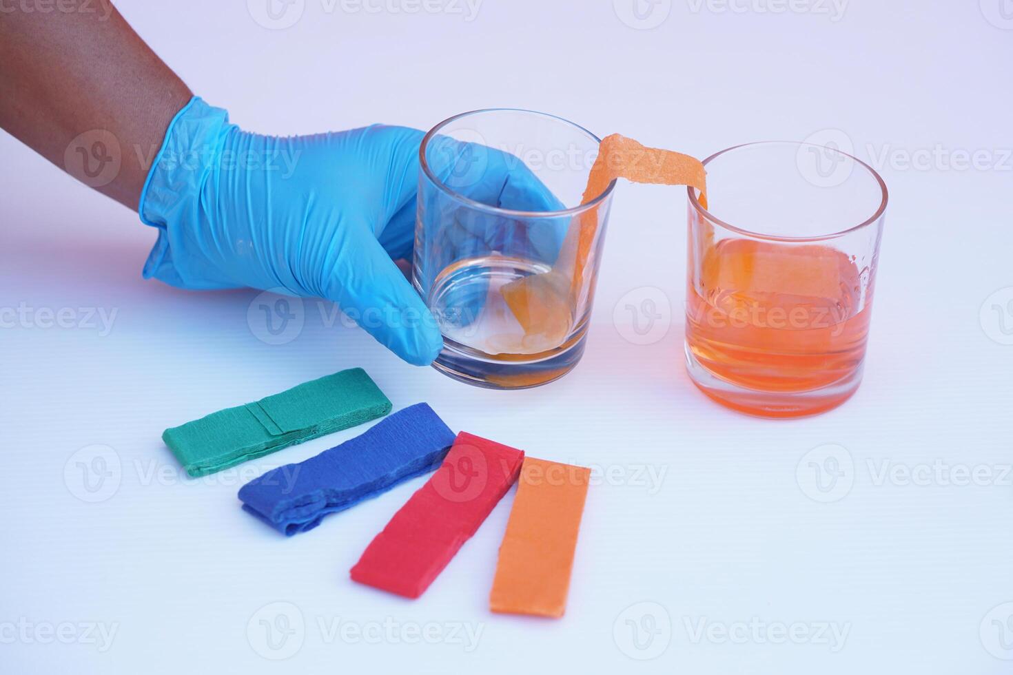 Hand wear blue glove, hold glass of color paper strip to absorb water to another glass.Concept, science lesson activity. Easy experiment for learning. Teaching education materials. Learning design photo