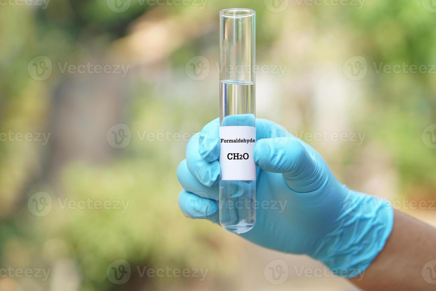 Close up hand wear blue glove, holds test tube of Formaldehyde liquid with molecular formula CH2O. Concept, chemical substance, colorless, toxic, strong-smell and flammable photo