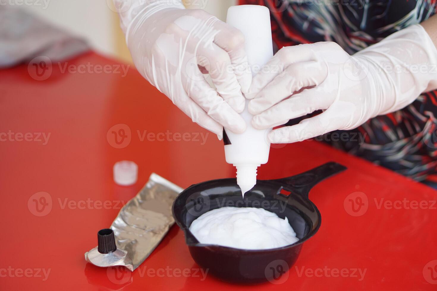 Close up hands wears gloves, squeezes dye hair color cream from tube in mix in black bowl before dying client's hair. Concept, hair beauty product for changing hair color by professional hairdresser. photo