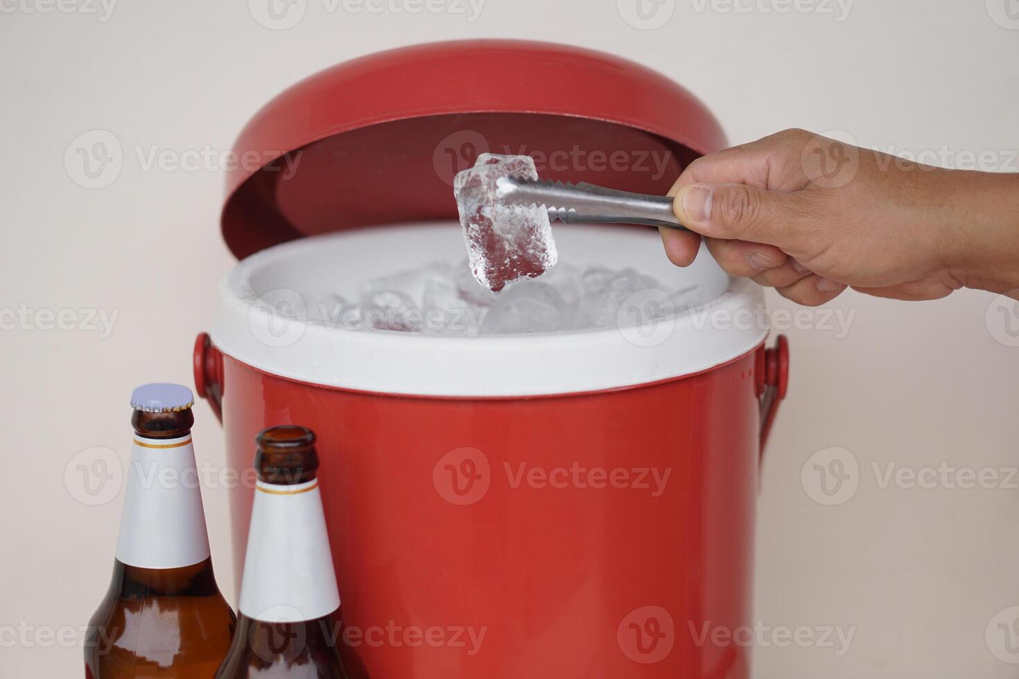 Close up hand hold tong to catch ice cube from red ice bucket cooler to prepare beverage. Concept, Mix drink for beer or alcohol beverage or cocktail with ice for more testy. photo