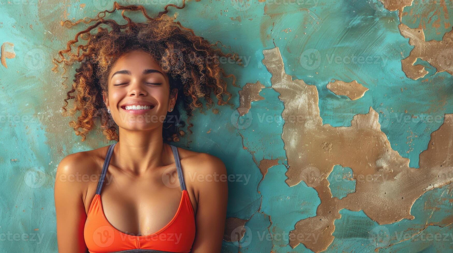 A woman wearing an orange bikini stands in front of a blue wall photo