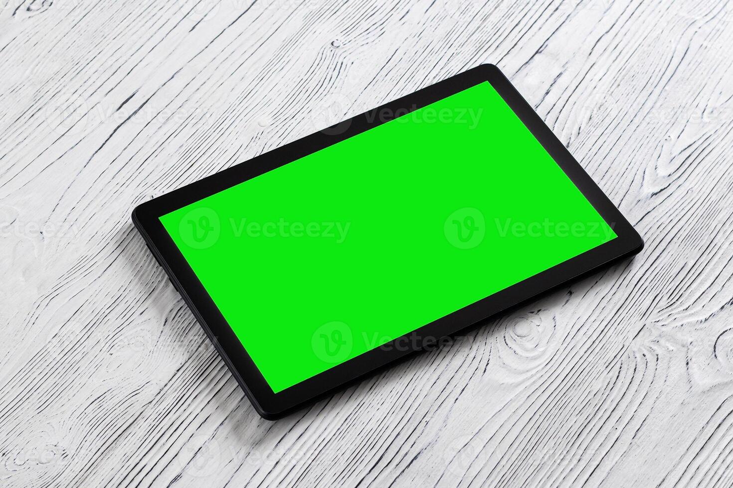 Black tablet with green screen on a wooden table mock up. Copy space chroma key display. photo