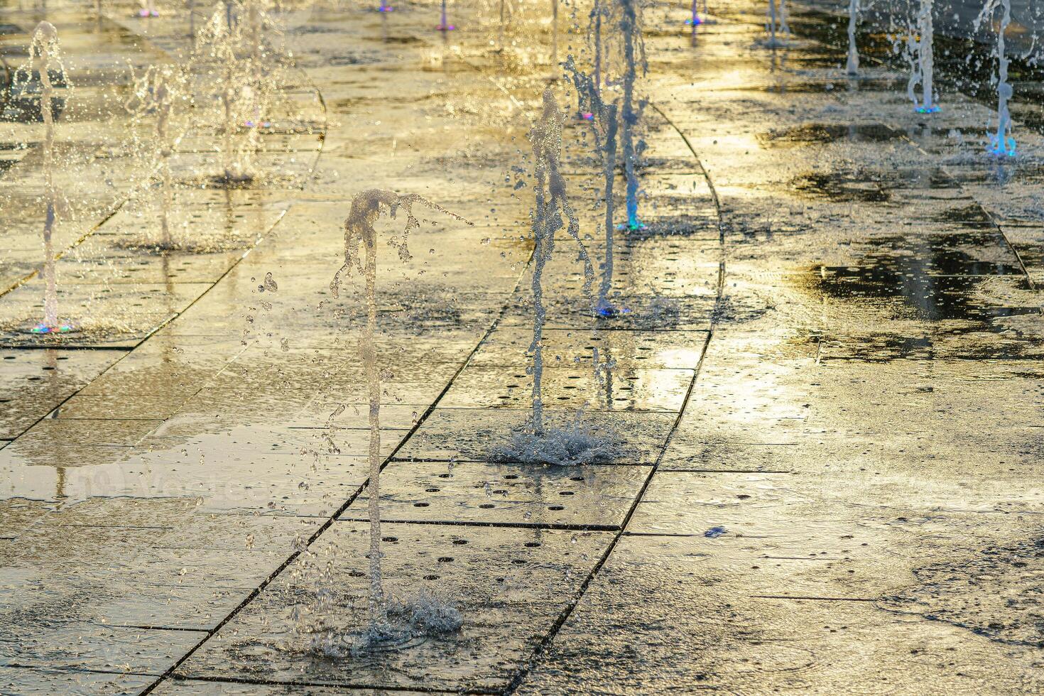 Small fountains on the sidewalk, illuminated by sunlight at sunset or sunrise at summertime. photo