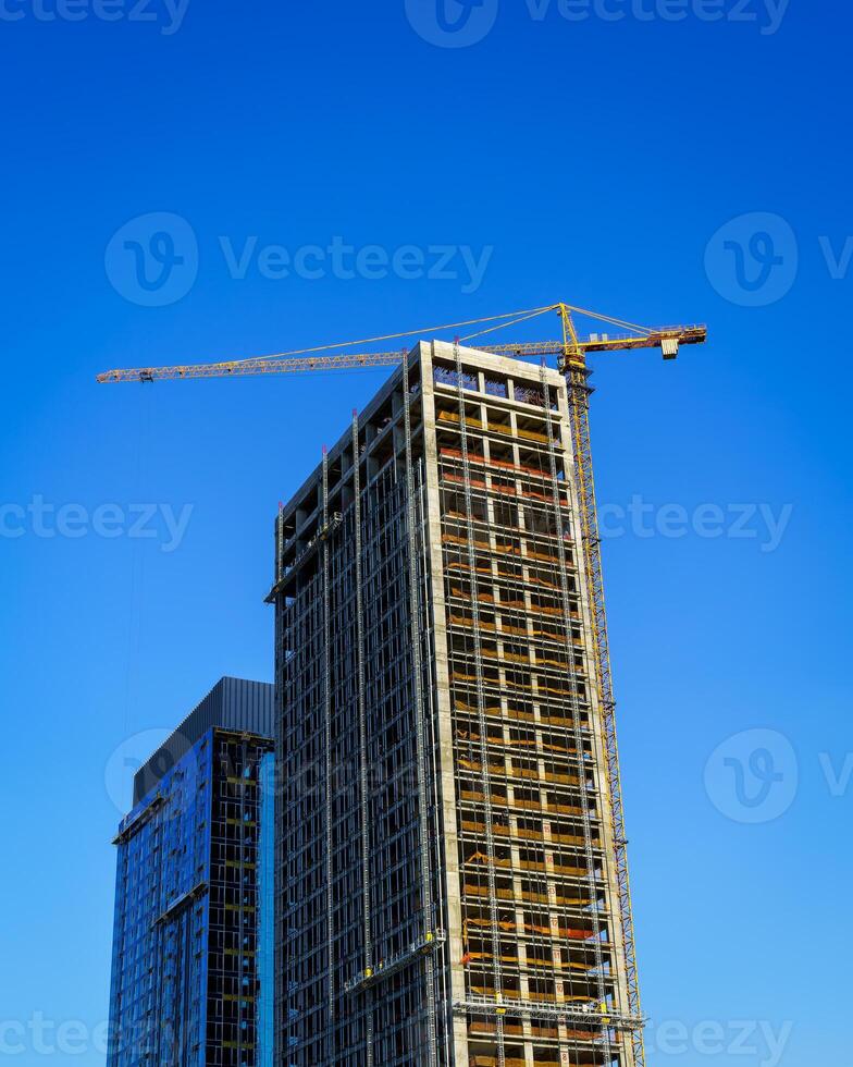 A crane building a modern skyscraper against a blue sky. Construction site. photo