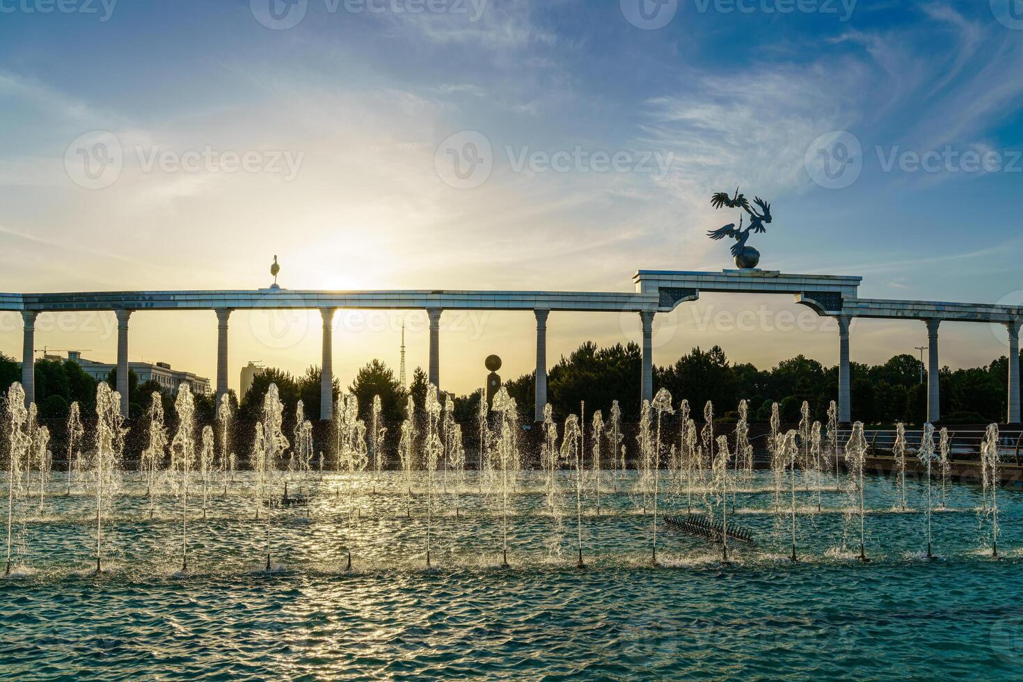 Memorial and rows of fountains illuminated by sunlight at sunset or sunrise in the Independence Square at summertime, Tashkent. photo