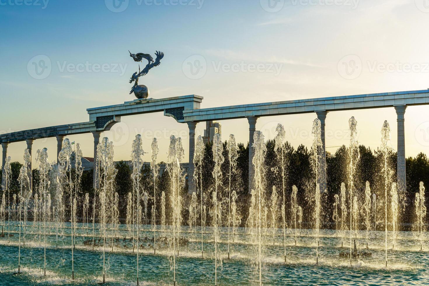 monumento y filas de fuentes iluminado por luz de sol a puesta de sol o amanecer en el independencia cuadrado a Hora de verano, Taskent. foto