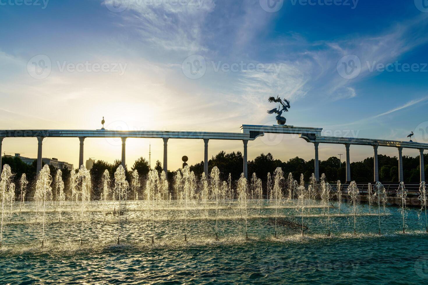 monumento y filas de fuentes iluminado por luz de sol a puesta de sol o amanecer en el independencia cuadrado a Hora de verano, Taskent. foto