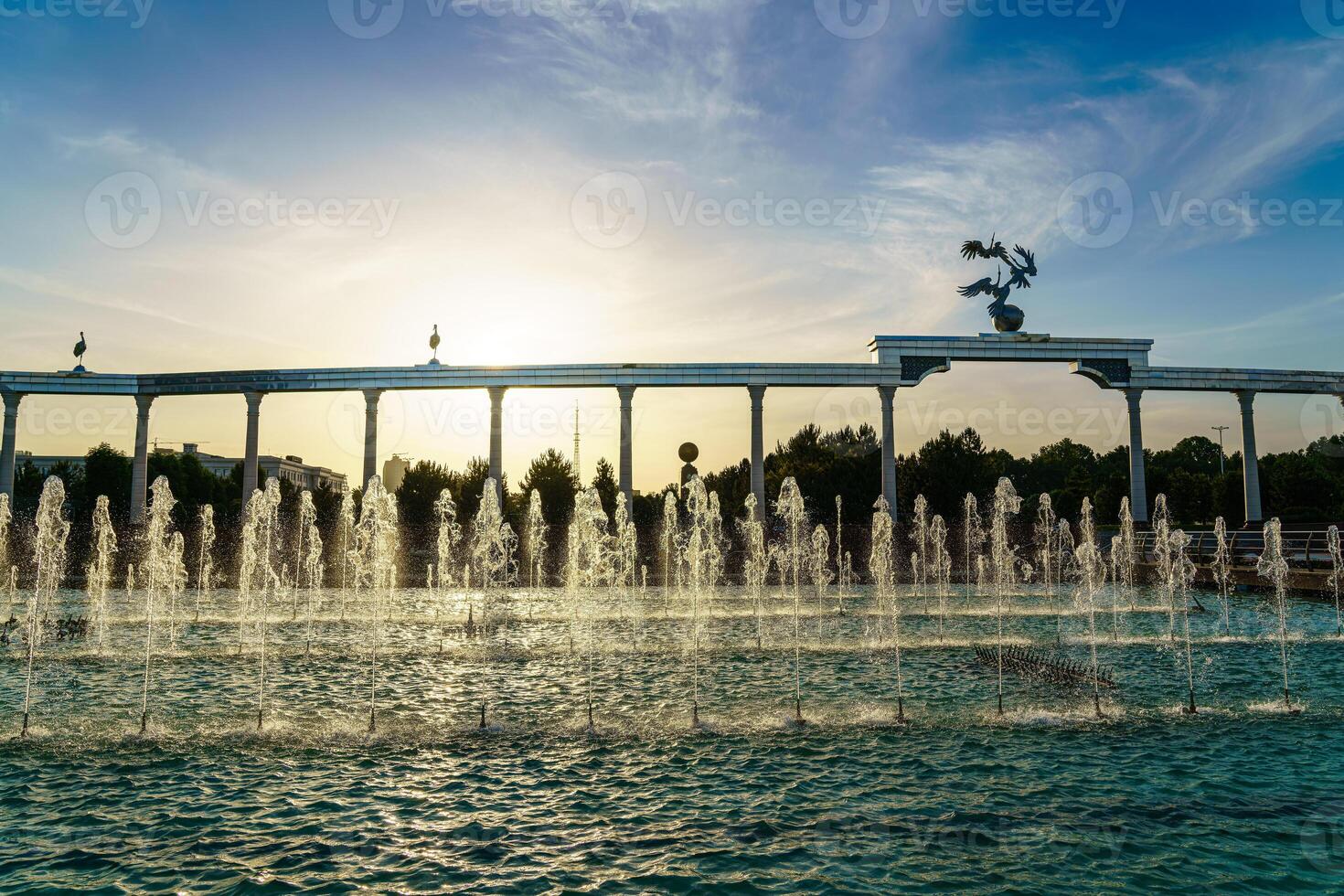 monumento y filas de fuentes iluminado por luz de sol a puesta de sol o amanecer en el independencia cuadrado a Hora de verano, Taskent. foto