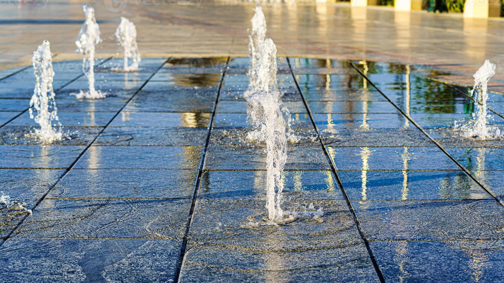 corrientes de salpicaduras pequeño fuentes en mojado pavimentación losas, iluminado por el Dom en un verano. foto