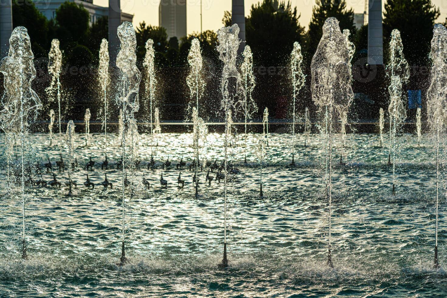 Fountains illuminated by sunlight at sunset or sunrise in the park at summertime. photo