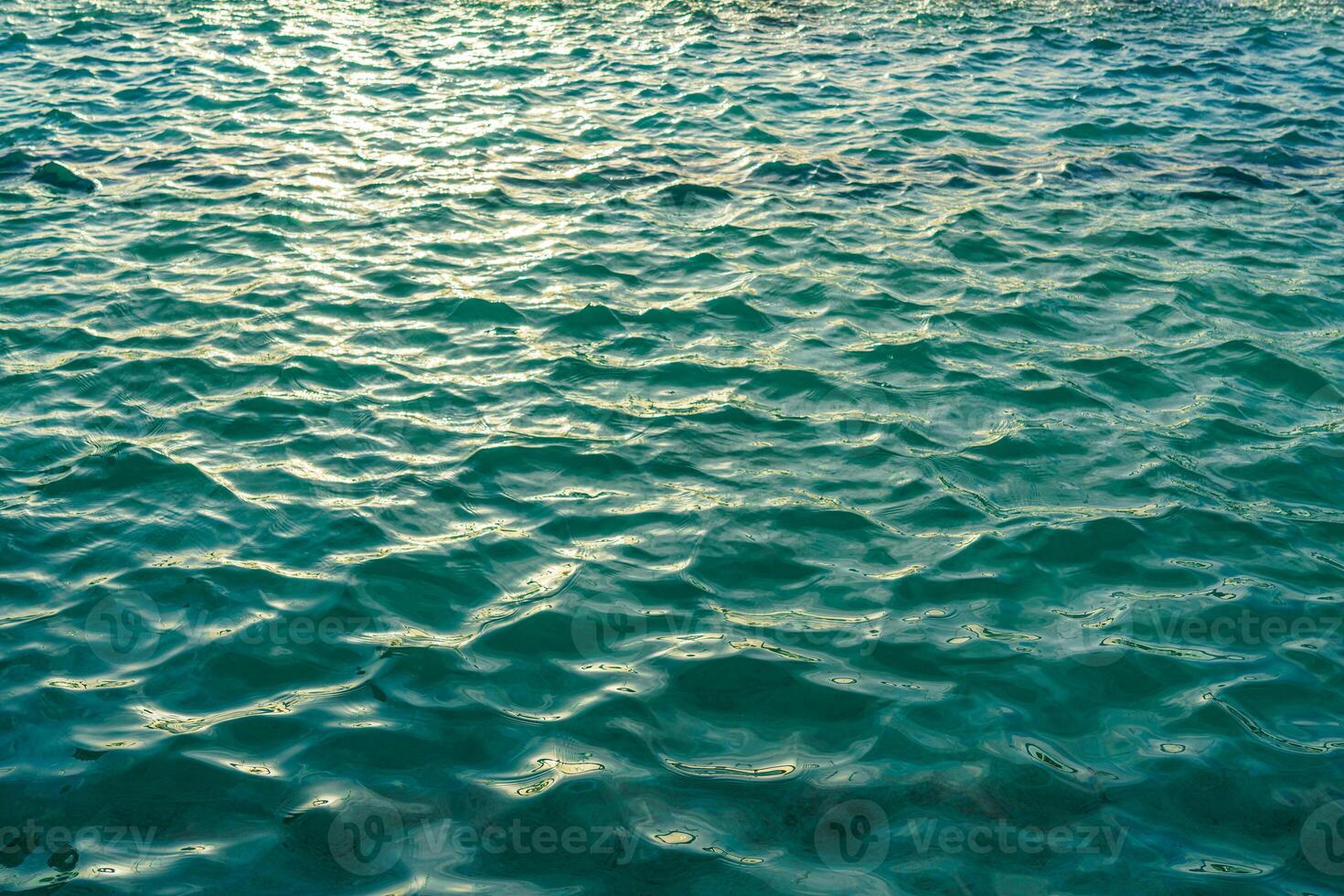 The texture of the waves in turquoise color, illuminated by the sun at sunset or dawn. Nature background. photo